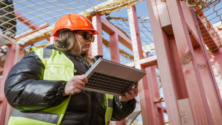 Building consent officer on a building site in a hardhat using a laptop to check building work