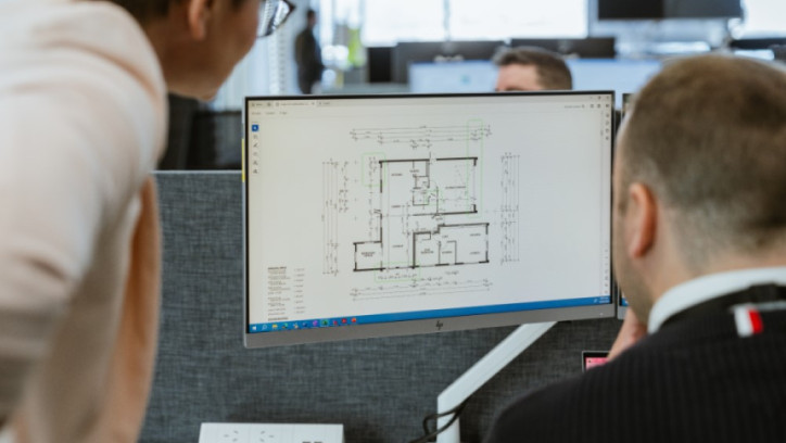 Over the shoulder view between 2 people at a desk checking a building plan on a computer screen