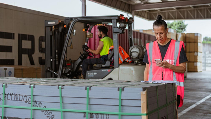 Woman in high-vis checking building product information on a cell phone.
