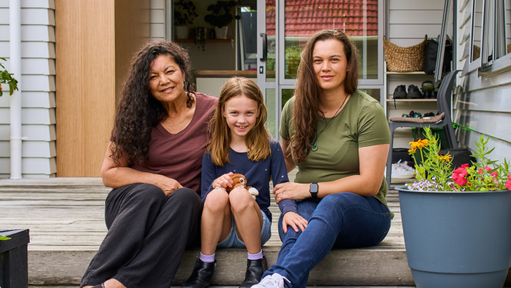 Family photo of 2 adults sitting either side a child on the doorstep of a house.